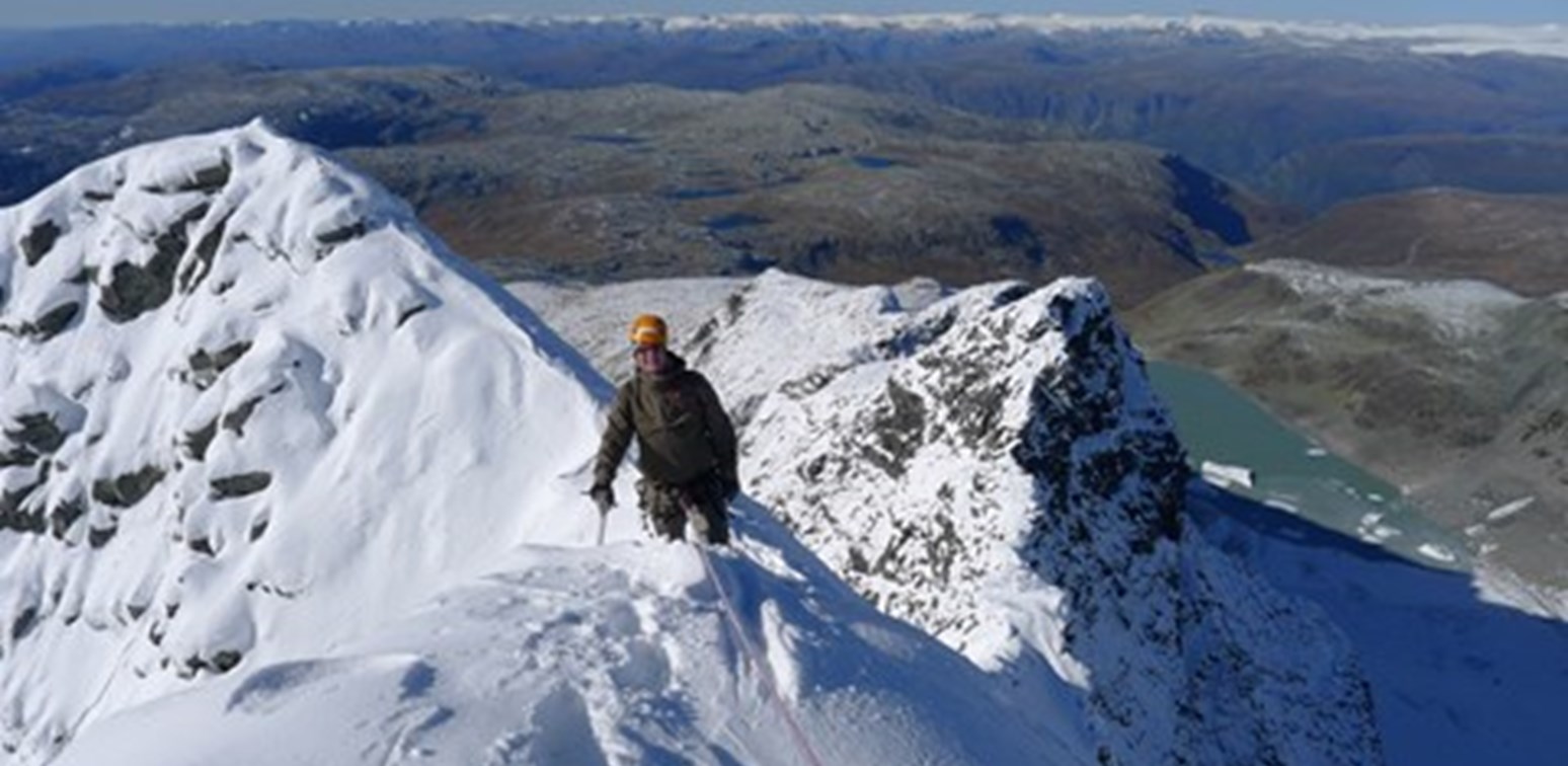 En person på tur med stegjern og isøks på vinterdekt fjell.