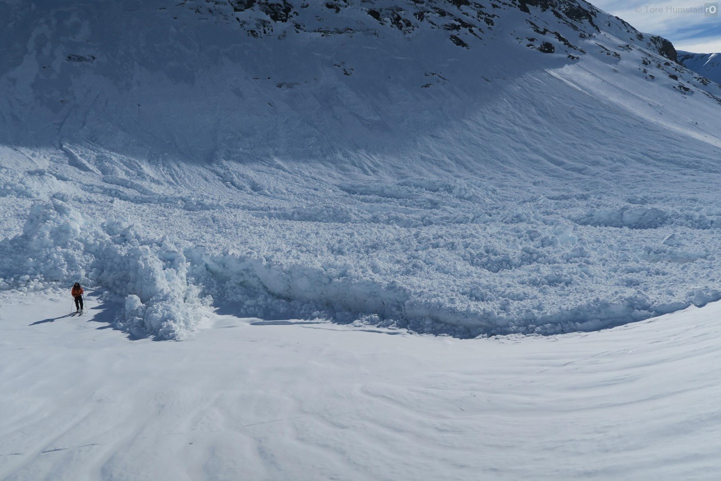 En skigåere står ved siden av skredavsetningene til et svært stort vått flakskred.